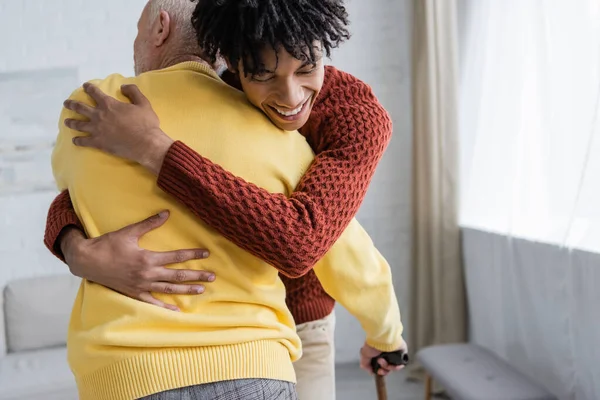 Happy African American Man Hugging Senior Grandparent Walking Cane Home — Stock Fotó