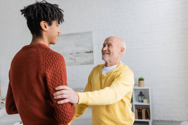 Positive senior granddad touching blurred african american grandson at home 