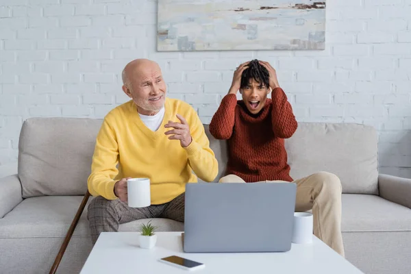 Smiling Pensioner Holding Cup Devices Amazed African American Grandson Home — Stock Fotó