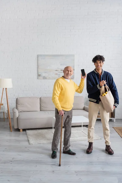 Cheerful Pensioner Holding Smartphone African American Grandson Food Home — Foto de Stock