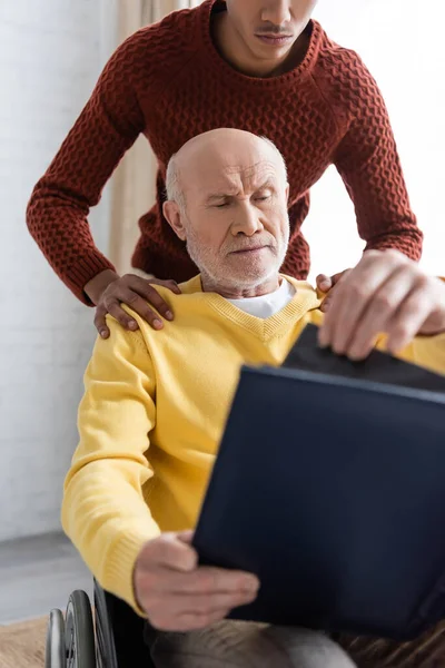 African American Man Hugging Granddad Wheelchair Holding Blurred Photo Album — Fotografia de Stock