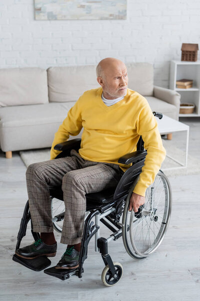 Пожилой человек смотрит в сторону, сидя в инвалидной коляске дома