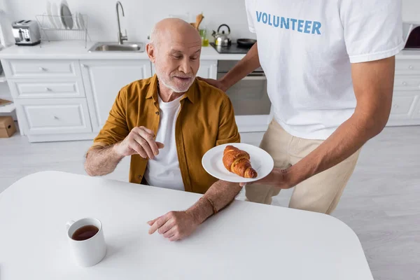 African American Volunteer Holding Croissant Senior Man Cup Tea Home — Foto de Stock