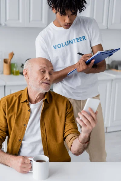 Senior Man Holding Smartphone Cup African American Volunteer Clipboard Home — ストック写真