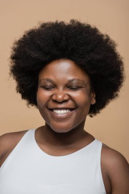portrait of cheerful african american plus size woman with closed eyes isolated on beige