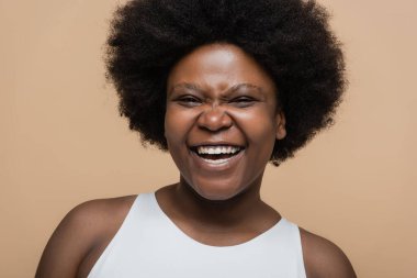 portrait of joyful african american plus size woman isolated on beige