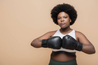 curly african american plus size woman with boxing gloves isolated on beige