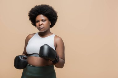 serious african american plus size woman with boxing gloves isolated on beige