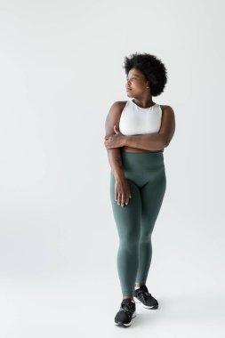 full length of pensive curly african american plus size woman in sportswear standing on white 