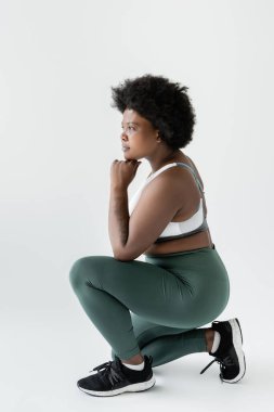 full length of curly african american plus size woman in sportswear sitting on white 