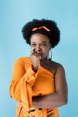 tattooed and worried african american body positive woman isolated on blue