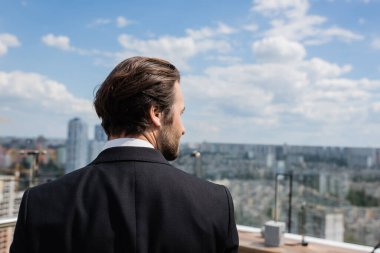Side view of brunette groom looking away on terrace 
