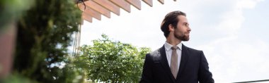 Side view of elegant groom looking away on terrace outdoors, banner 