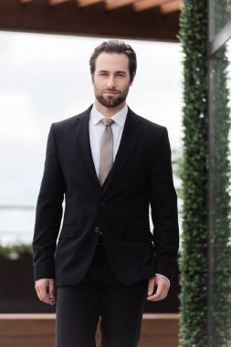 Bearded groom in suit looking at camera on terrace of restaurant 