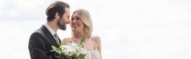 Cheerful groom hugging bride with bouquet outdoors, banner 