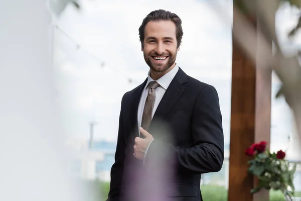 Cheerful groom in suit looking at camera outdoors
