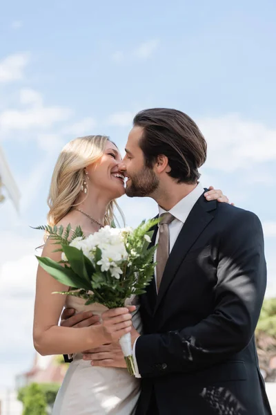 Side View Cheerful Newlyweds Holding Flowers Kissing Outdoors — Foto de Stock