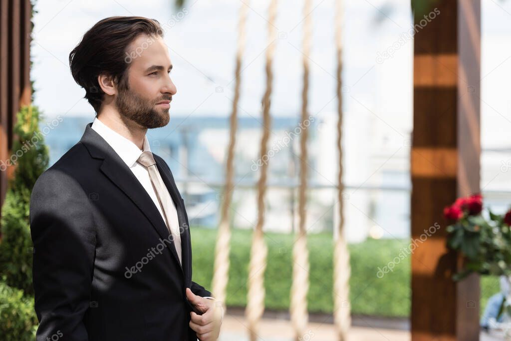 Side view of groom in elegant suit standing on terrace 