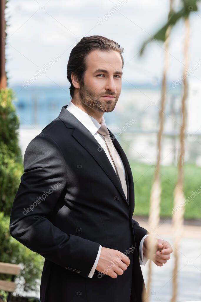 Elegant groom in black suit looking at camera on terrace 