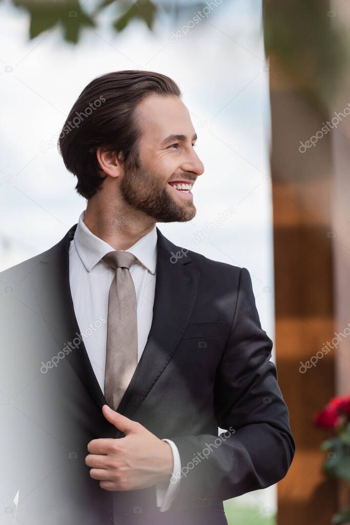 Side view of positive bearded groom in suit looking away outdoors 