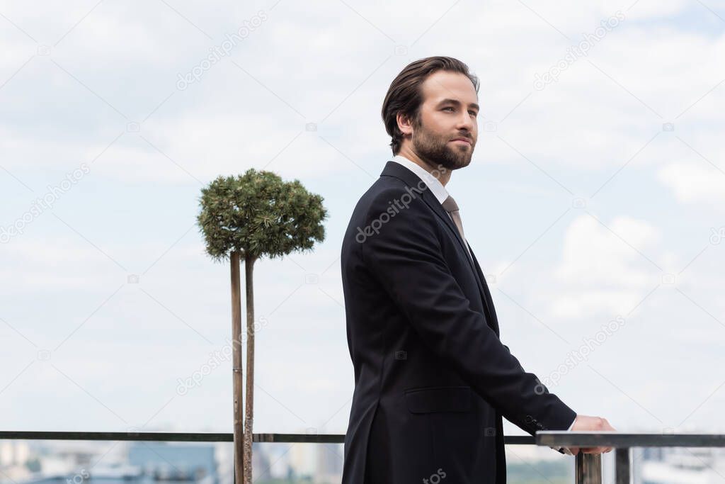 Young groom in black formal wear looking away on terrace