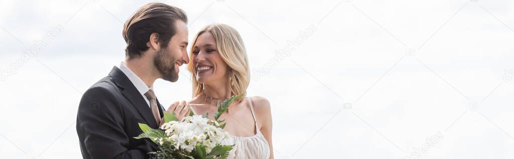 Cheerful groom hugging bride with bouquet outdoors, banner 