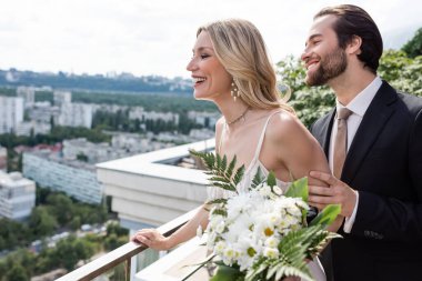 Side view of groom and wife with bouquet looking away from terrace 