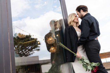 Low angle view of man kissing girlfriend with red roses on terrace of restaurant 