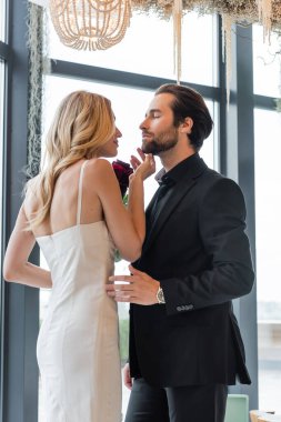 Blonde woman holding flowers and touching man in suit in restaurant  clipart