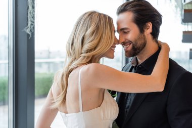 Side view of smiling blonde woman embracing boyfriend in suit in restaurant 