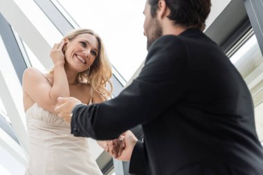 Low angle view of blurred man holding hand of cheerful girlfriend in dress in restaurant 