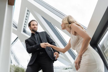 Low angle view of young man in suit holding hand of blonde girlfriend in restaurant 