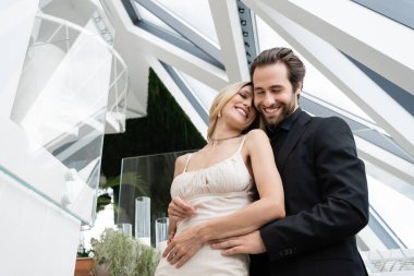 Low angle view of smiling elegant couple closing eyes while hugging in restaurant 
