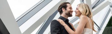 Low angle view of elegant couple smiling at each other while hugging in restaurant, banner 