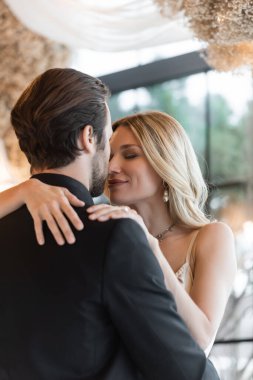 Blonde woman hugging boyfriend in suit in restaurant 