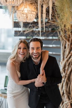 Happy romantic couple hugging and looking at camera under decorative tree in restaurant 