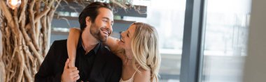 Cheerful woman hugging and looking at boyfriend in restaurant, banner 