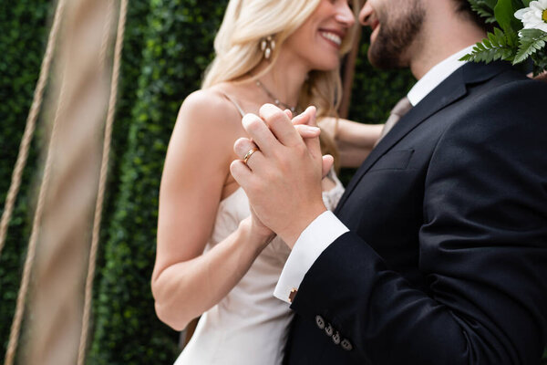 Cropped view of blurred newlyweds holding hands on terrace of restaurant 