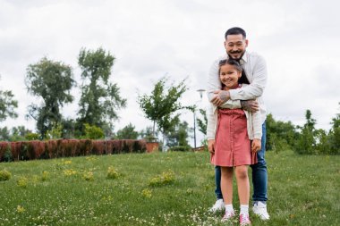 Smiling asian dad hugging preteen daughter in park 