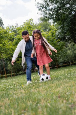 Asian family playing soccer on grass in summer park 