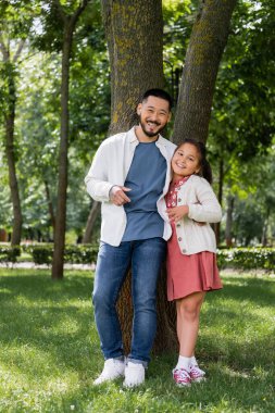 Cheerful asian family looking at camera near tree in park 