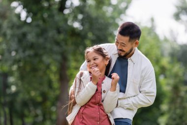 Bearded asian father playing with daughter in park 
