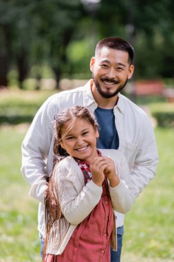 Happy asian father and daughter looking at camera in park 