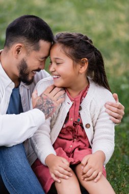Happy asian parent hugging daughter on lawn in park 