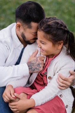 Positive asian man hugging preteen daughter in summer park 