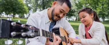 Smiling asian family playing acoustic guitar in park, banner 