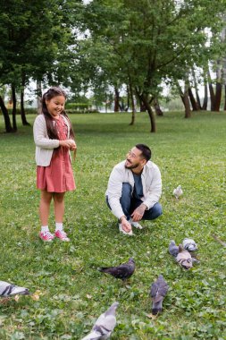 Asian parent and daughter feeding birds in summer park 