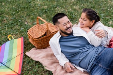 Happy asian dad lying near daughter and wicket basket in park  clipart