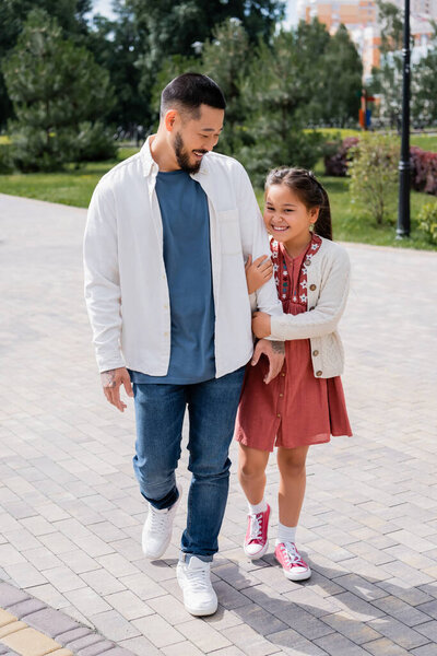 Cheerful father and asian daughter walking in park 