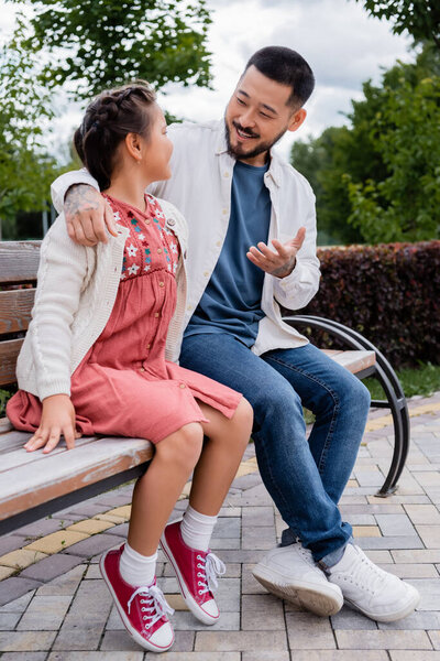 Asian parent talking to preteen daughter on bench in park 